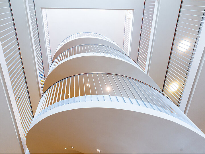 DSR_Asset_Real_Estate_Consulting Eine weiße Spindeltreppe, innenliegend, Blick nach oben