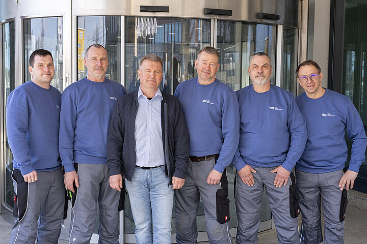 DSR_Asset_Technischer_Service Foto von einer Männergruppe im Bereich Gebäudetechnik, vor einer Drehtür stehend