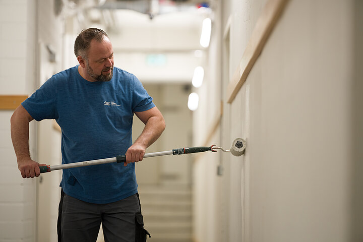 Infrastrukturelle Facility Services von DSR Asset Management Haustechnikerfährt mit einer Malerrolle über die Wand