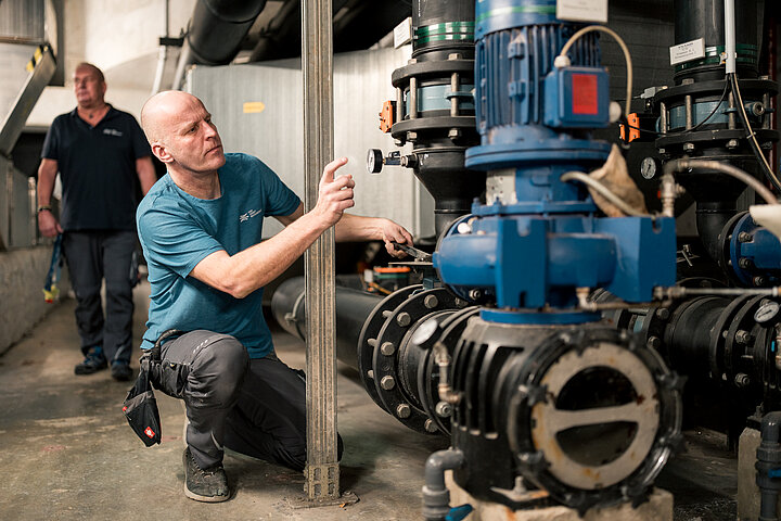Technische Facility Services von DSR Asset Management Kniender Haustechniker kontrolliert Wasserkreislauf an einem Gerät